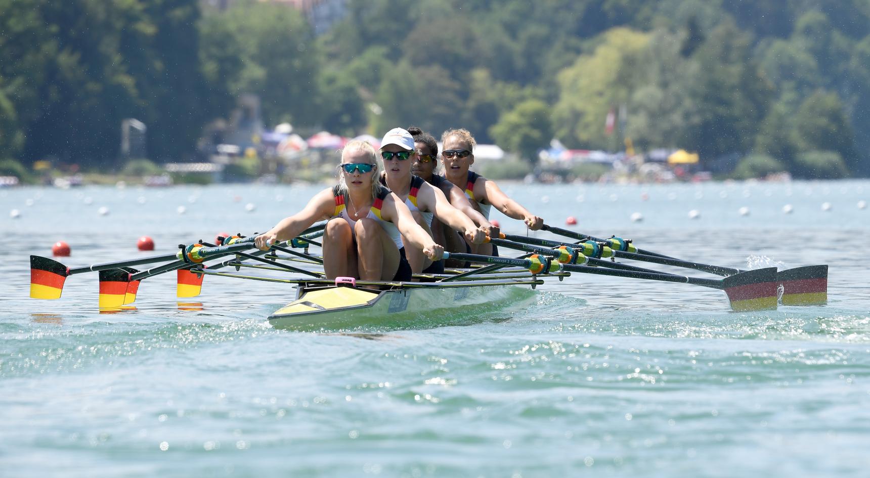 Vier Frauen im Ruderrennboot mit aufgestellten Ruderblättern die in den Nationalfarben Schwarz-Rot-Gold gestrichen sind